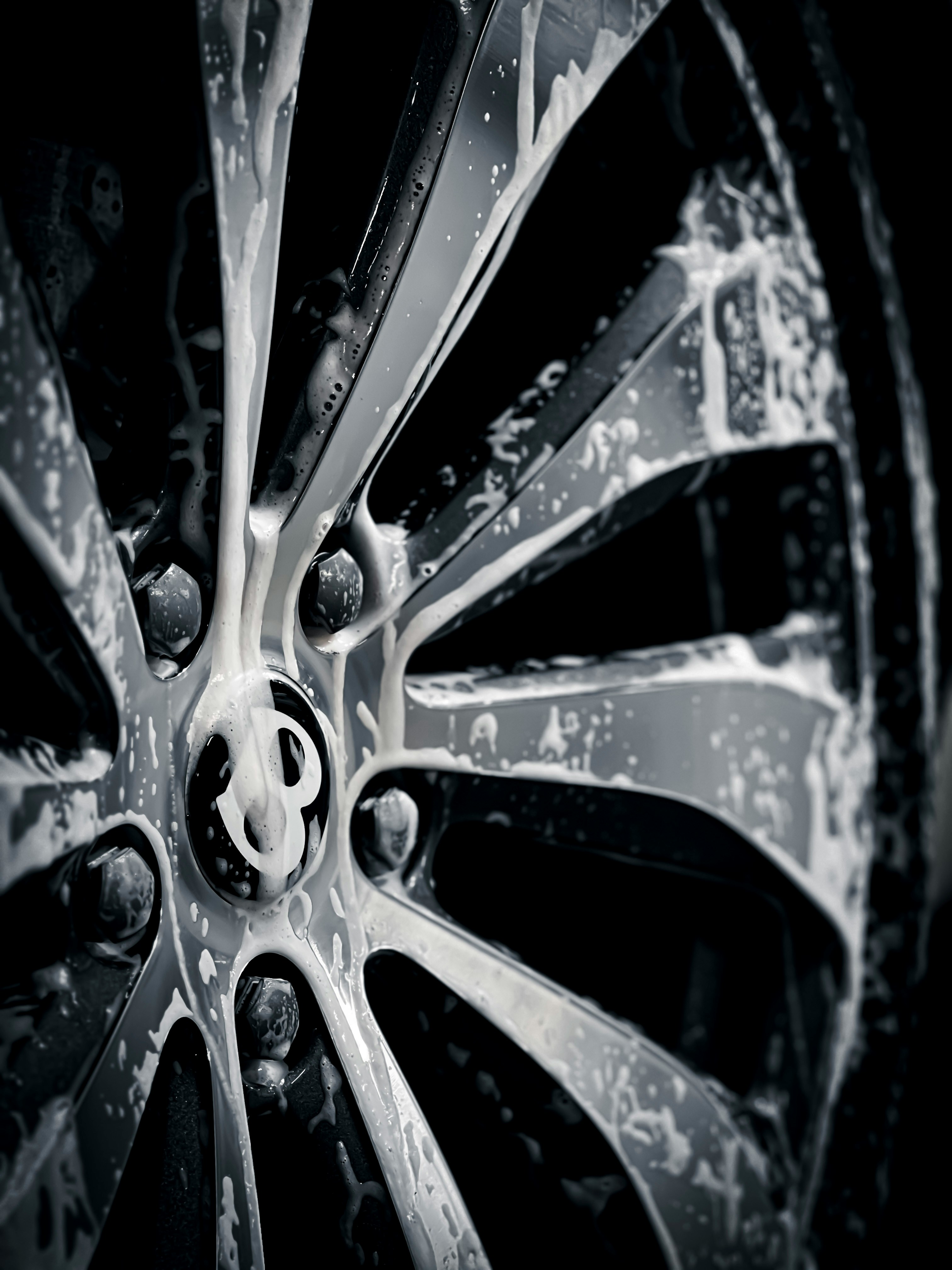 close up photo of a bentley wheel with soap running down the wheel. Black and white.
