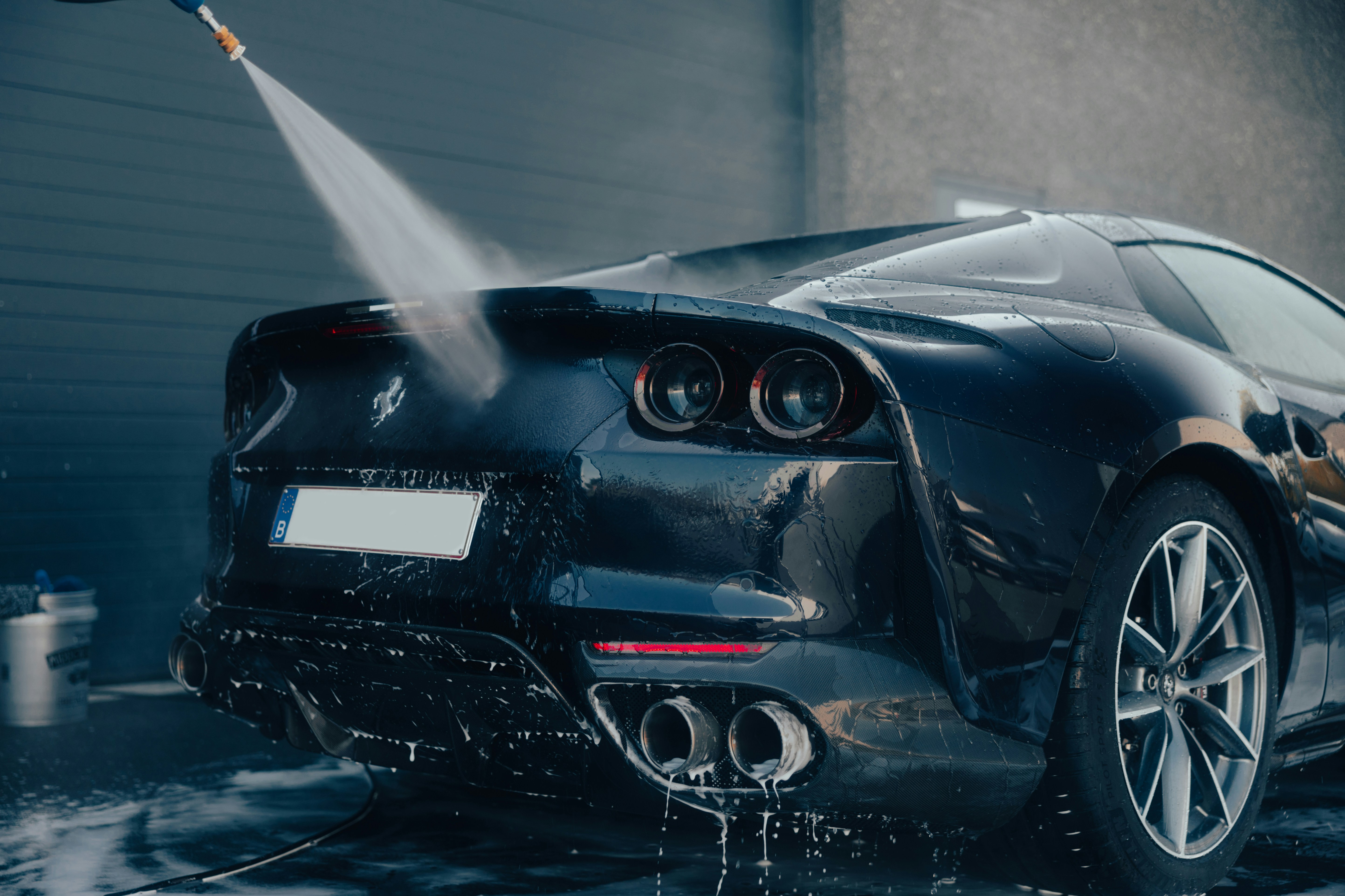 A black Ferrari being jetwashed from behind as soap falls off the car